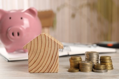 Photo of House model, stacked coins, piggy bank and notebook on wooden table, selective focus