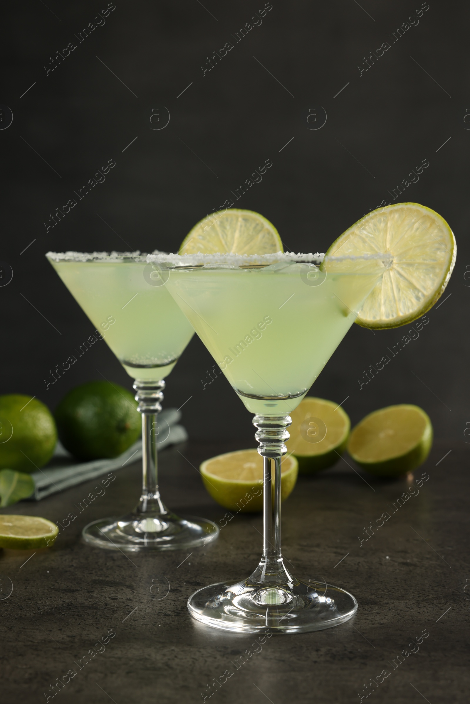 Photo of Delicious Margarita cocktail in glasses and limes on grey table