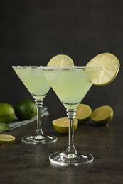 Delicious Margarita cocktail in glasses and limes on grey table