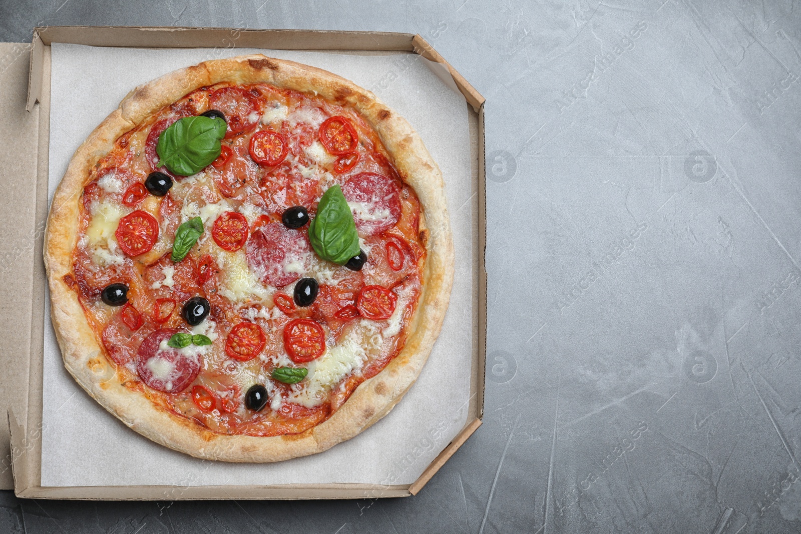 Photo of Delicious pizza Diablo in cardboard box on grey table, top view. Space for text