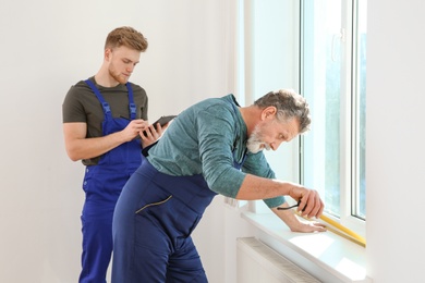 Photo of Service men measuring window for installation indoors