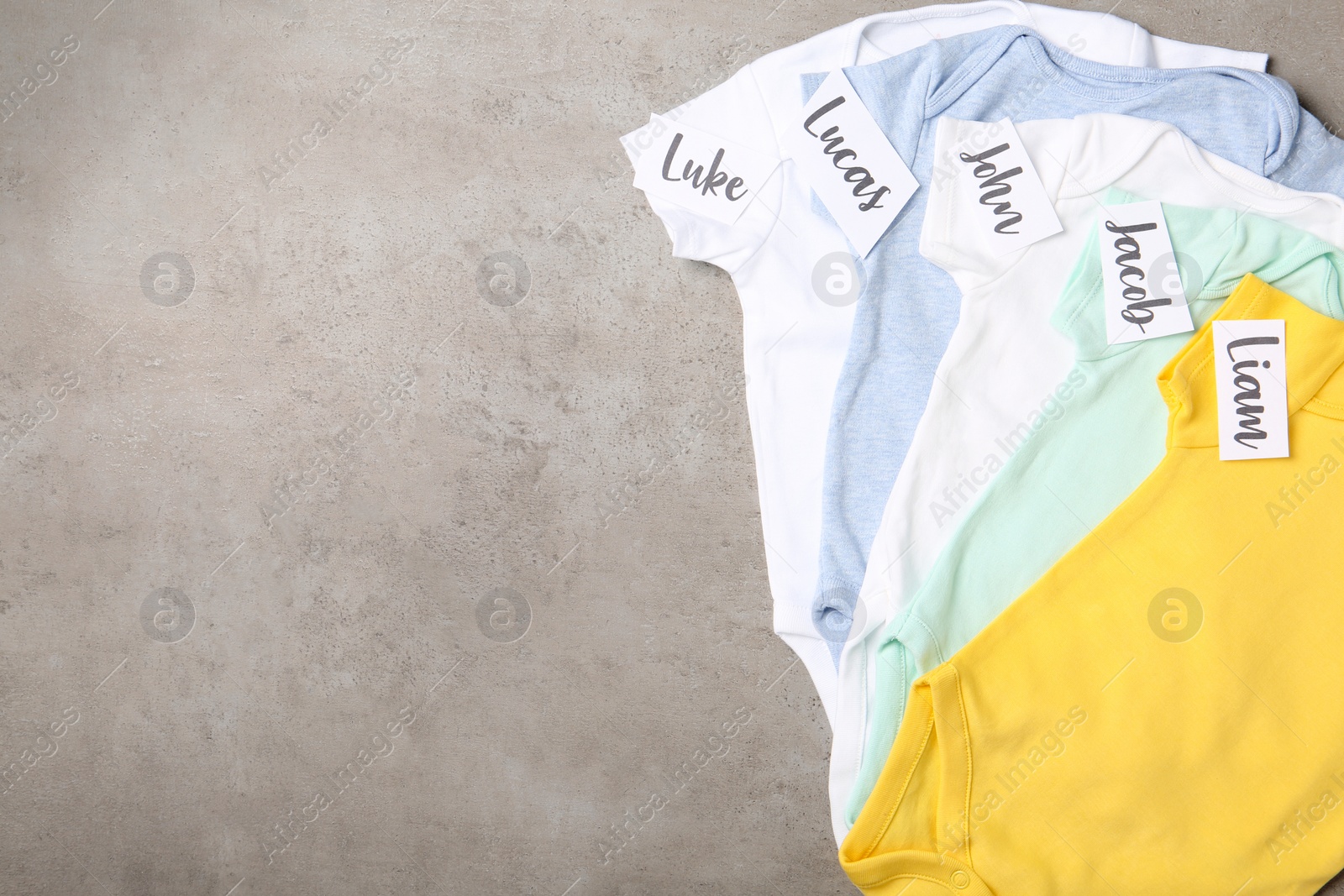 Photo of Bodysuits with different baby names on grey background, flat lay. Space for text