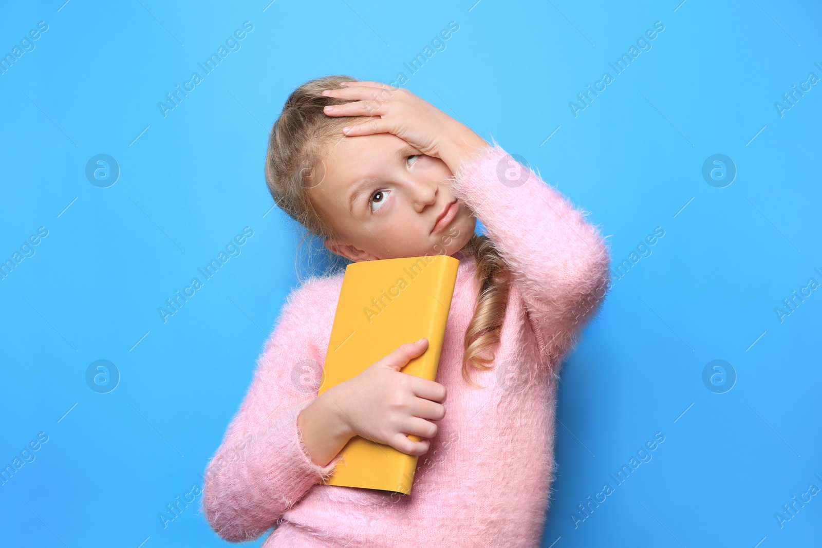 Photo of Emotional little girl with book on light blue background
