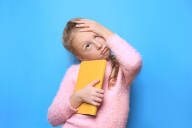 Emotional little girl with book on light blue background