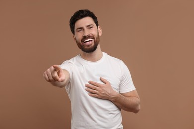 Handsome man pointing at something and laughing on light brown background