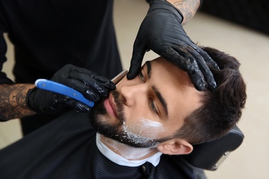 Photo of Professional hairdresser shaving client with straight razor in barbershop