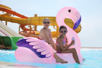 Photo of Mother and daughter with inflatable flamingo mattress in swimming pool at water park. Family vacation