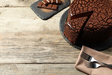 Photo of Delicious truffle cake, chocolate pieces and forks on wooden table, space for text