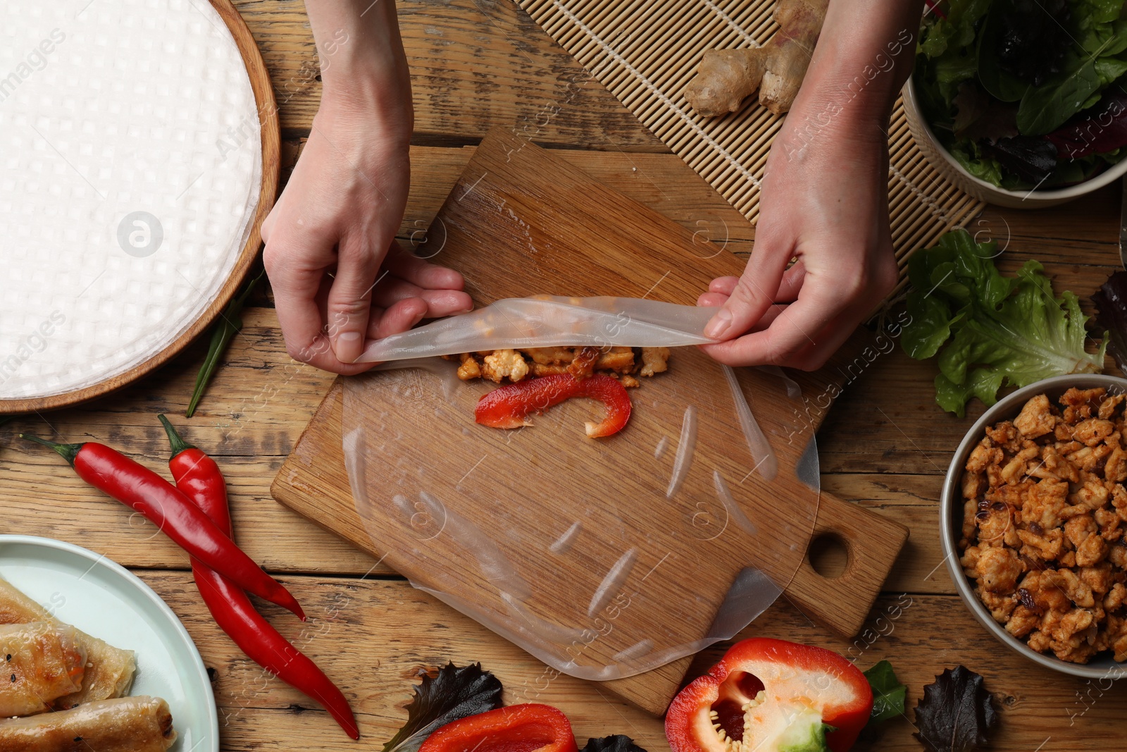 Photo of Woman making tasty spring roll at wooden table, top view