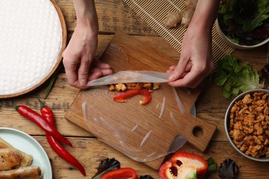 Photo of Woman making tasty spring roll at wooden table, top view