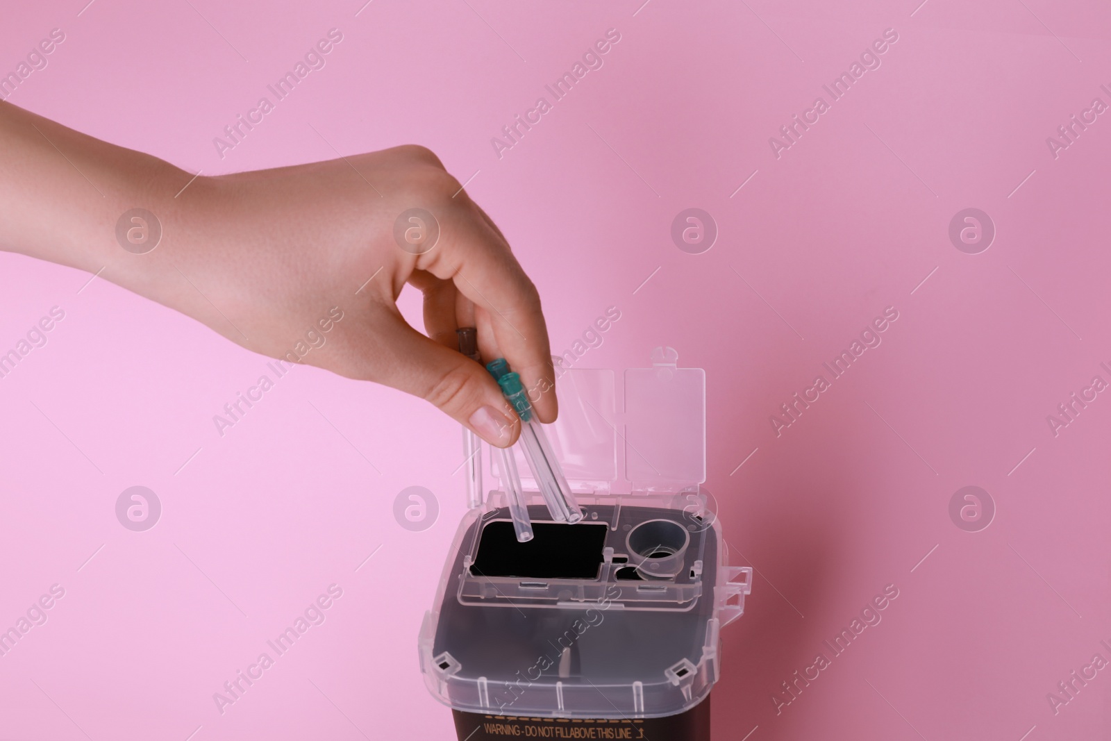 Photo of Woman throwing used syringe needles into sharps container  on pink background, closeup