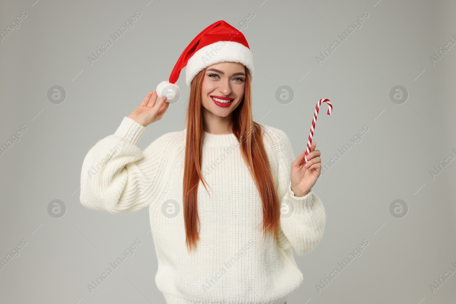 Photo of Young woman in Santa hat with candy cane on light grey background. Christmas celebration