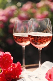 Glasses of rose wine on table in blooming garden