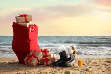 Photo of Santa's boots, cocktail, sunglasses and bag with presents on beach. Christmas vacation