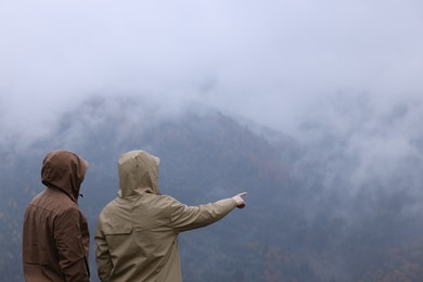 Photo of Man and woman in raincoats enjoying mountain landscape