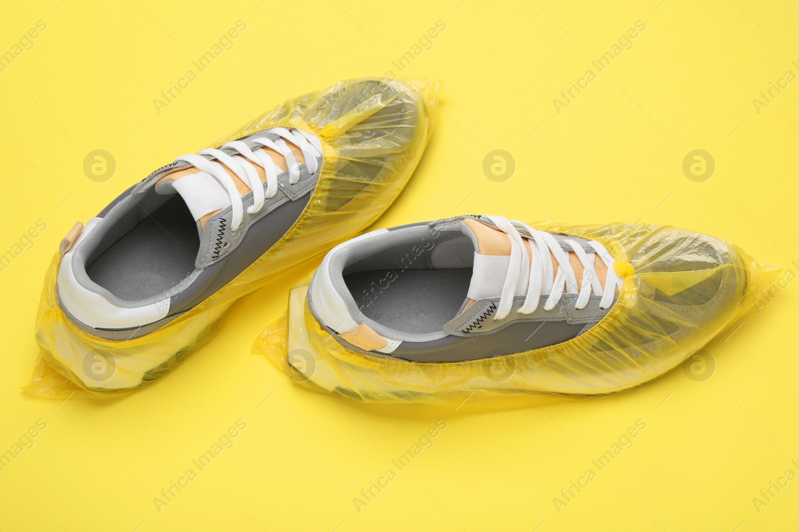 Photo of Sneakers in shoe covers on yellow background, closeup