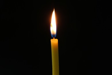 Photo of One burning church candle on dark background, closeup