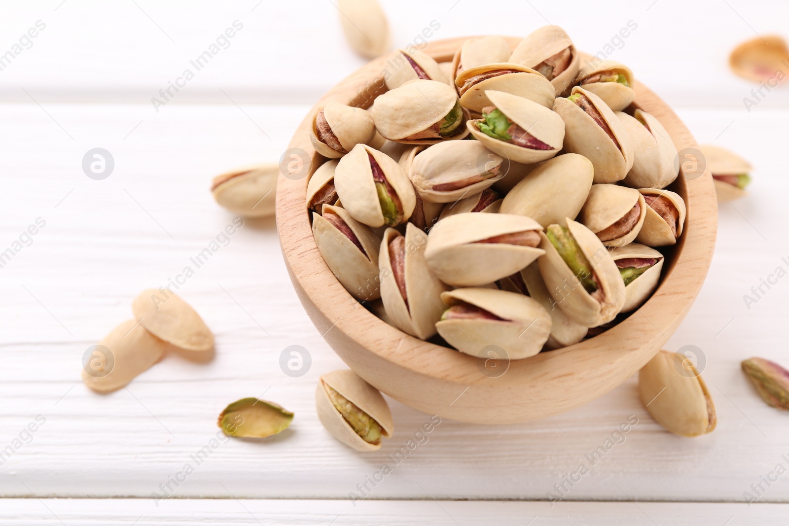 Photo of Tasty pistachios in bowl on white wooden table, closeup. Space for text