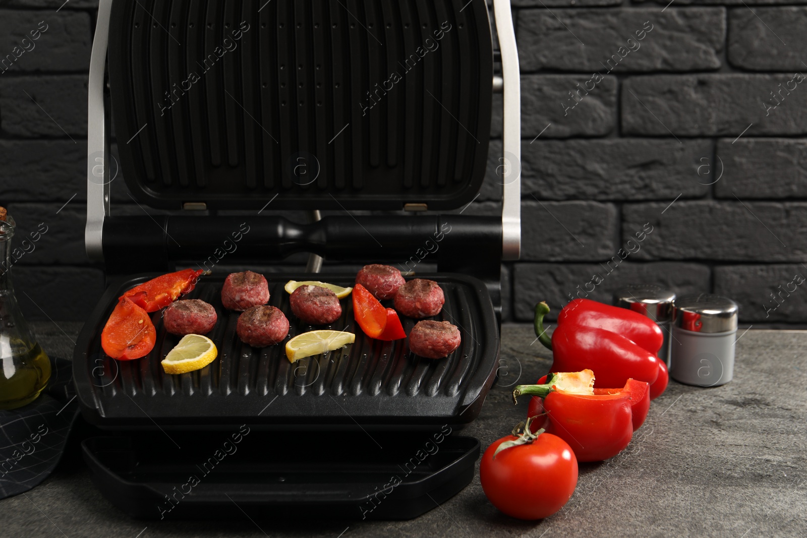 Photo of Electric grill with meat balls, bell peppers and lemon on grey textured table