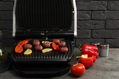 Photo of Electric grill with meat balls, bell peppers and lemon on grey textured table