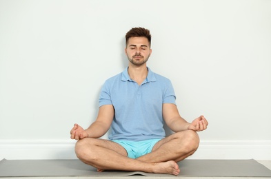 Photo of Young man practicing zen yoga near wall indoors