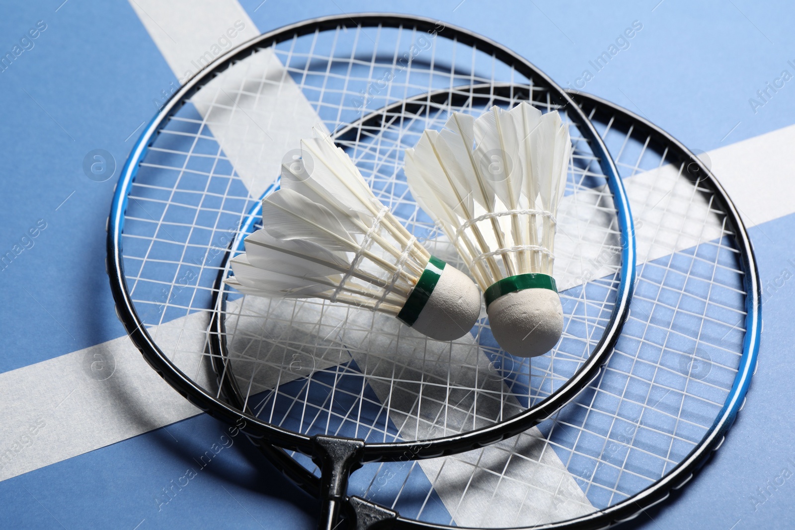 Photo of Feather badminton shuttlecocks and rackets on blue background, closeup