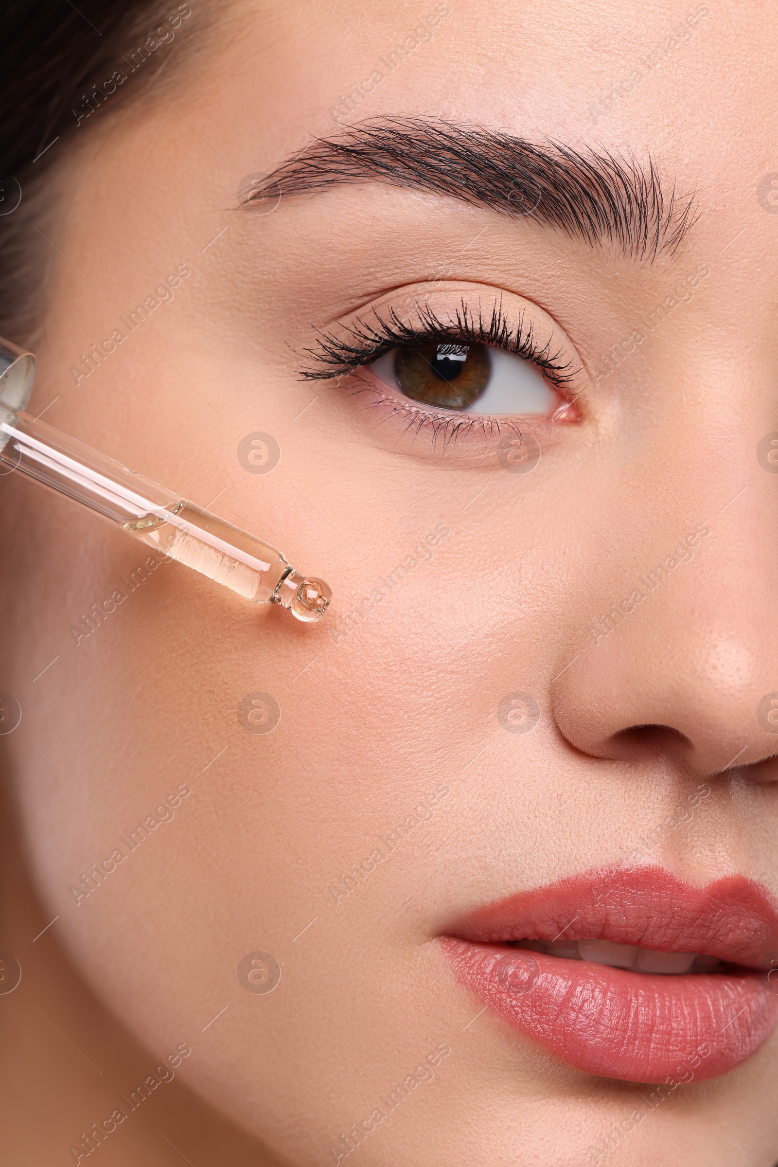 Photo of Young woman applying essential oil onto face, closeup