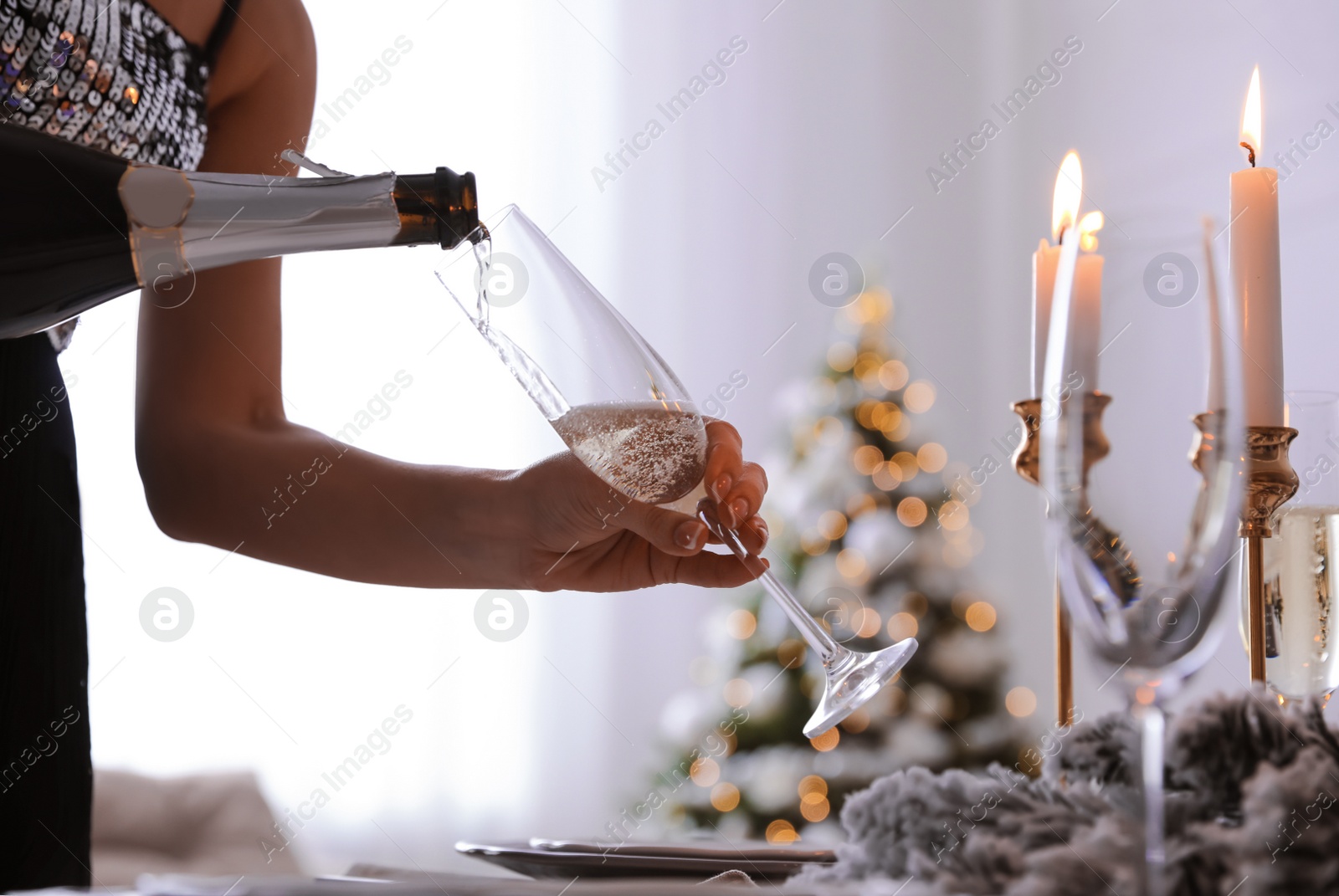 Photo of Woman pouring champagne into glass at home, closeup