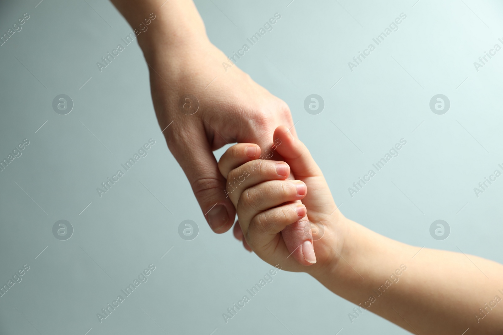 Photo of Mother and child holding hands on light blue background, closeup