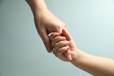 Mother and child holding hands on light blue background, closeup