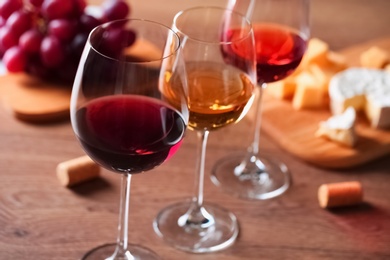 Photo of Glasses with different wines and appetizers on wooden table, closeup