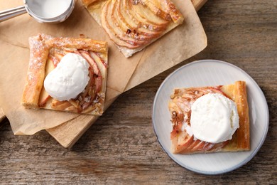 Pieces of freshly baked apple pie served with ice cream on old wooden table, flat lay