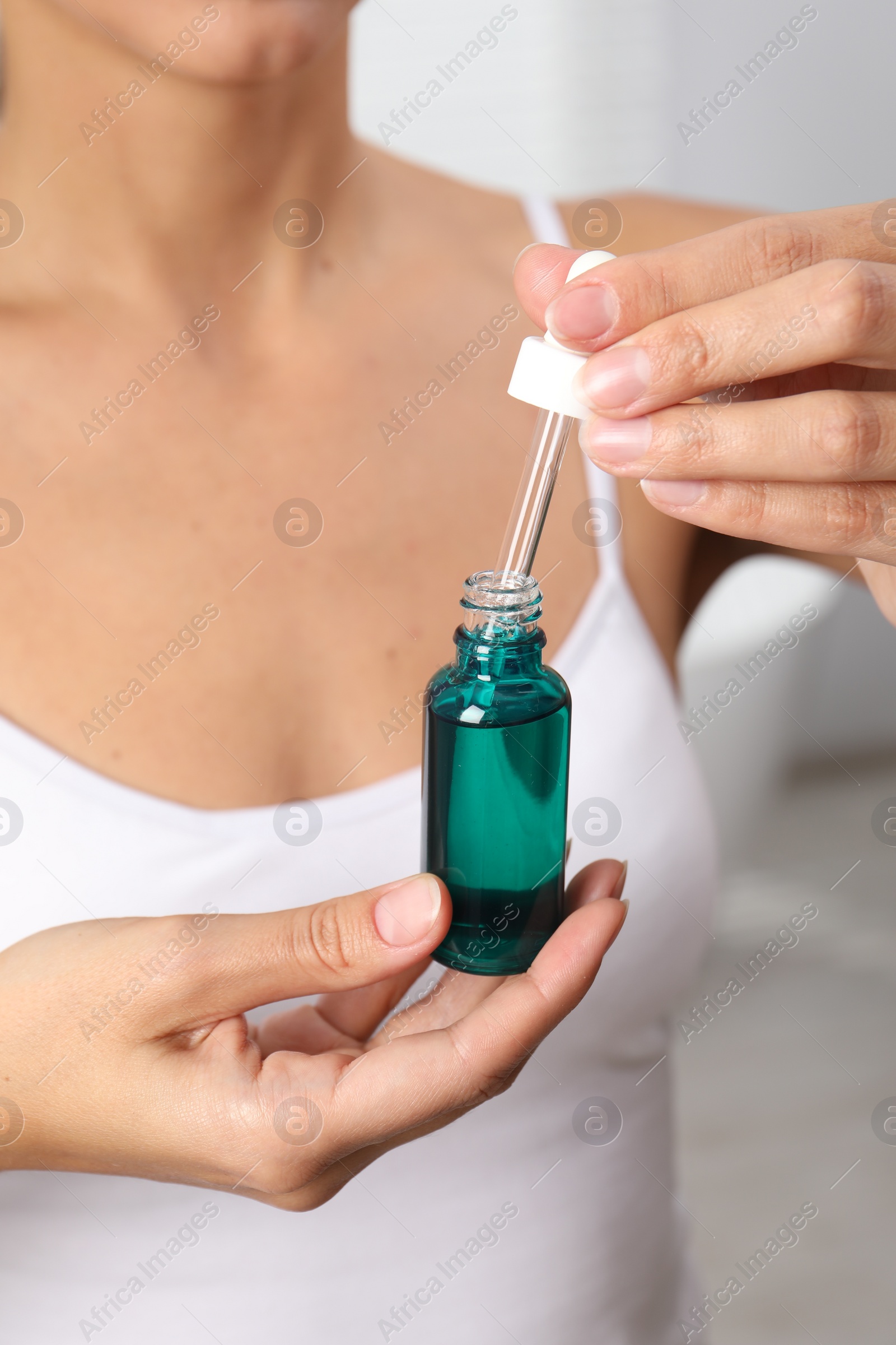 Photo of Woman with bottle of cosmetic serum on blurred background, closeup