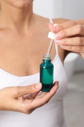 Woman with bottle of cosmetic serum on blurred background, closeup