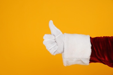 Photo of Santa Claus showing thumb up on yellow background, closeup of hand
