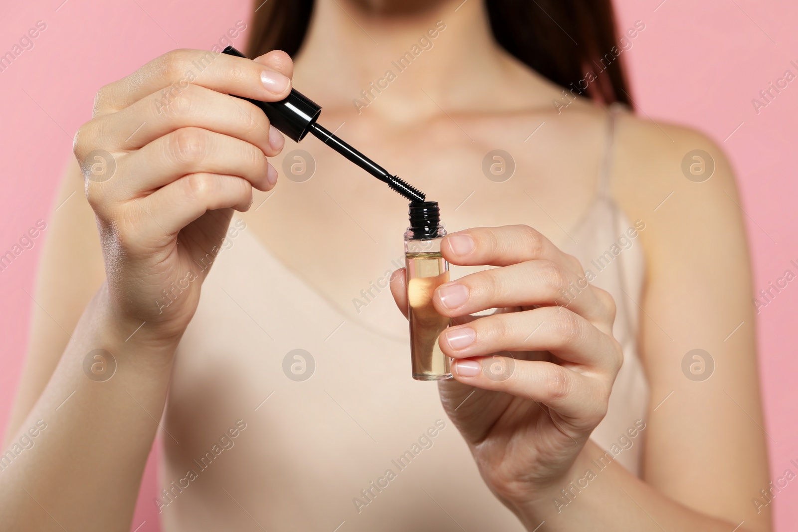 Photo of Young woman with eyelash oil on pink background, closeup