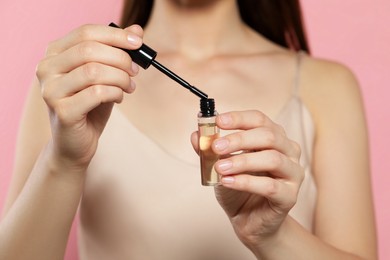 Young woman with eyelash oil on pink background, closeup