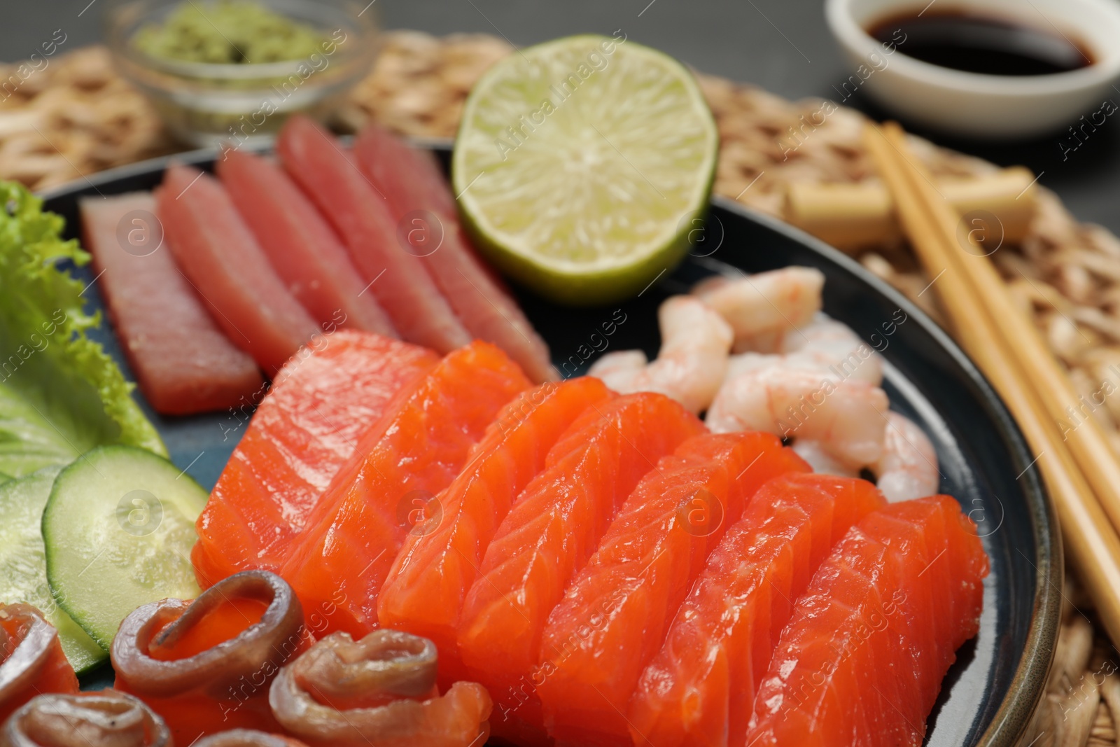 Photo of Tasty salmon slices, shrimp, cucumber and tuna on wicker mat, closeup. Delicious sashimi set