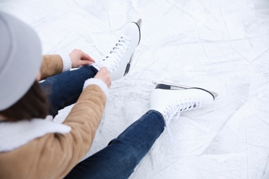 Woman lacing figure skate while sitting on ice rink, above view