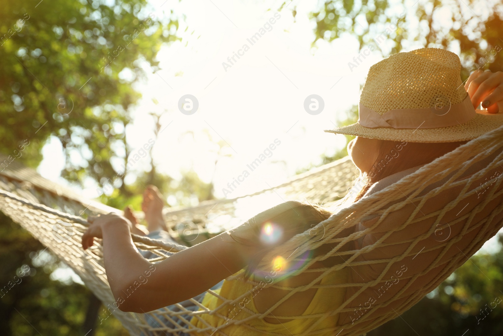 Photo of Young woman with hat resting in comfortable hammock at green garden