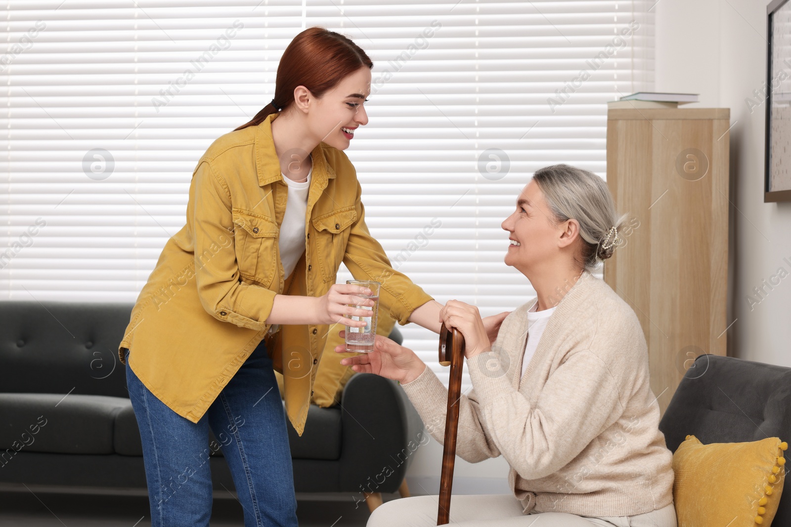 Photo of Caregiver giving water to senior woman with walking cane at home