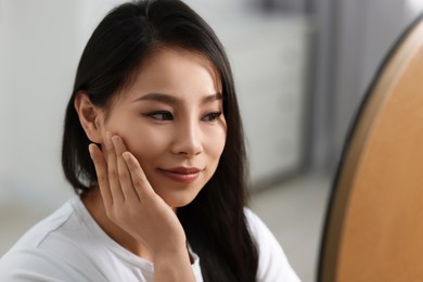 Woman with perfect skin looking at mirror indoors