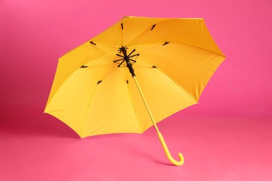 Photo of Stylish open yellow umbrella on pink background