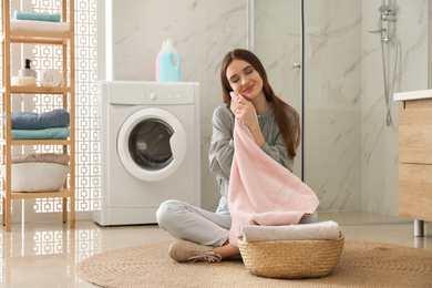 Photo of Happy woman with clean towel near washing machine in bathroom. Laundry day