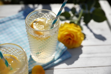 Glasses of refreshing lemonade and beautiful yellow rose on white wooden table. Space for text
