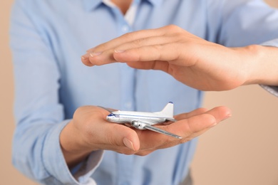 Photo of Insurance agent covering toy plane on color background, closeup. Travel safety concept