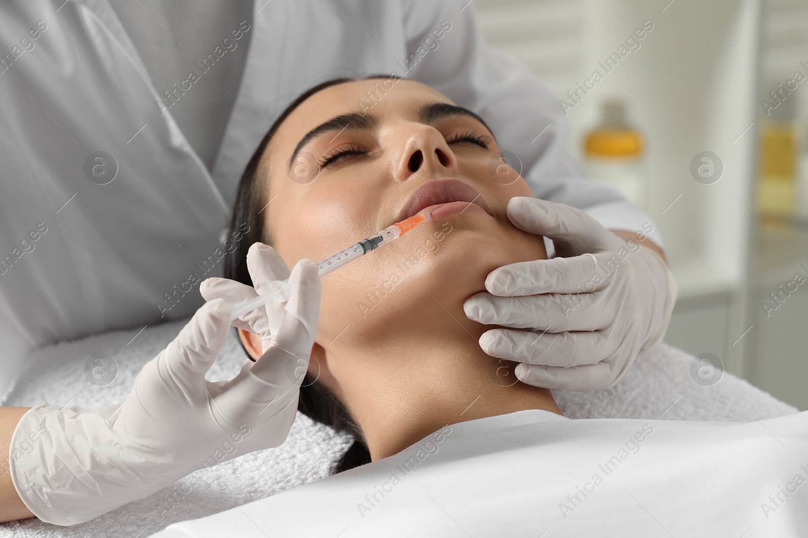 Photo of Doctor giving lips injection to young woman in clinic. Cosmetic surgery