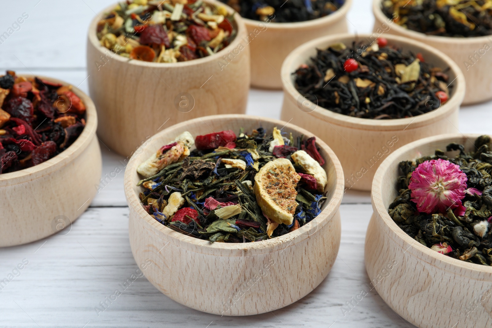 Photo of Different kinds of dry herbal tea in bowls on white wooden table