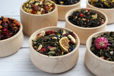 Photo of Different kinds of dry herbal tea in bowls on white wooden table