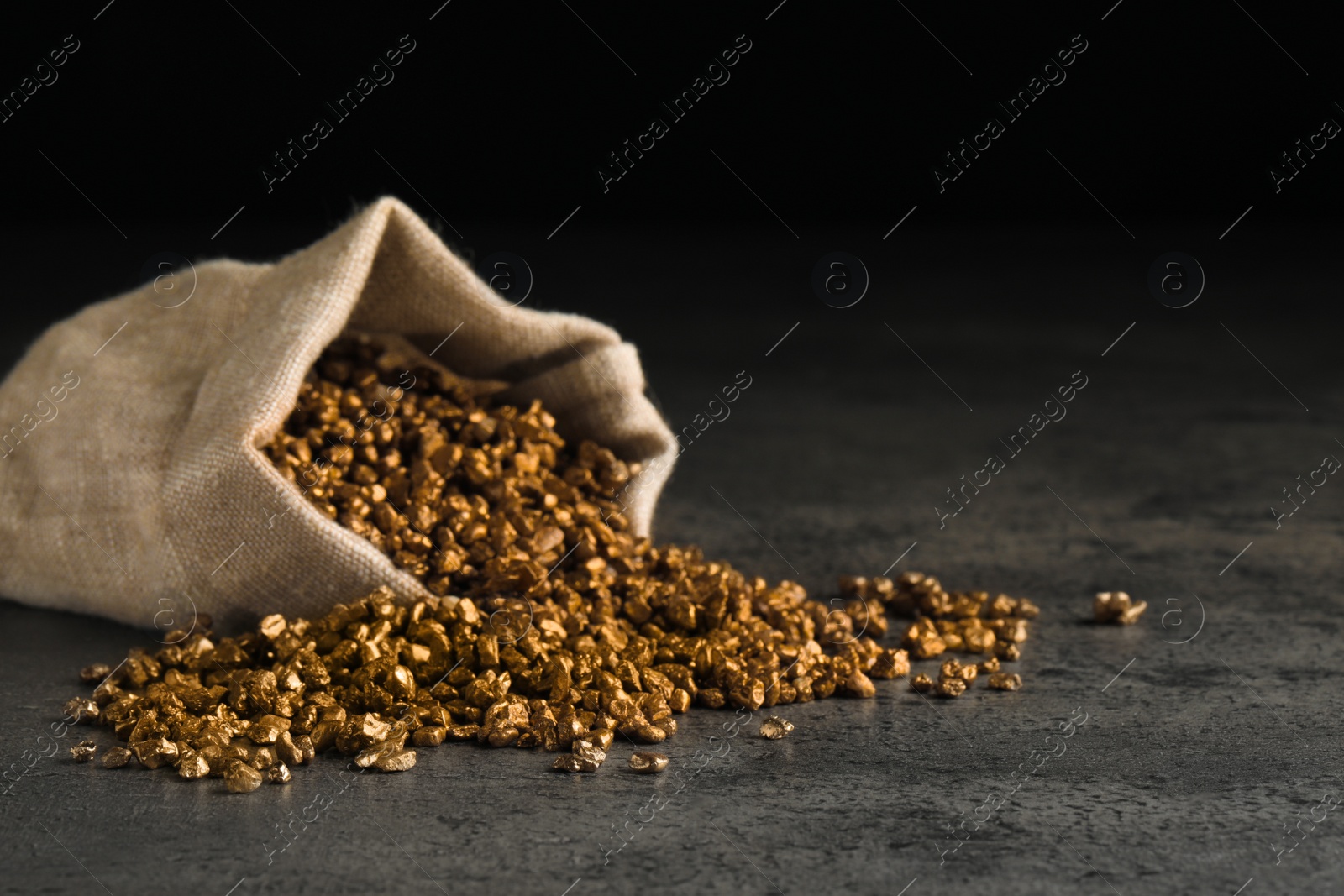 Photo of Overturned sack of gold nuggets on grey table against dark background, space for text